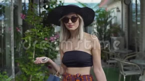 时尚的年轻女性戴着太阳镜帽子和裤子穿着时尚在露天购物中心购物视频的预览图