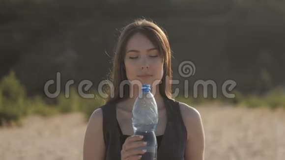 年轻的女性旅行者在炎热的沙地从大自然中的塑料瓶里喝水女孩渴望喝水视频的预览图