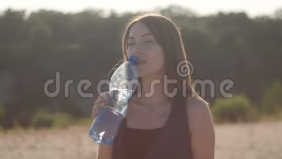 年轻的女性旅行者在炎热的沙地从大自然中的塑料瓶里喝水女孩渴望喝水视频的预览图