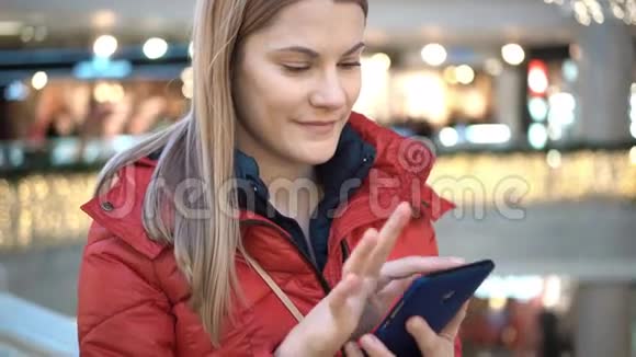 商场里有智能手机的漂亮女人浏览互联网与朋友交流冬天的外套视频的预览图