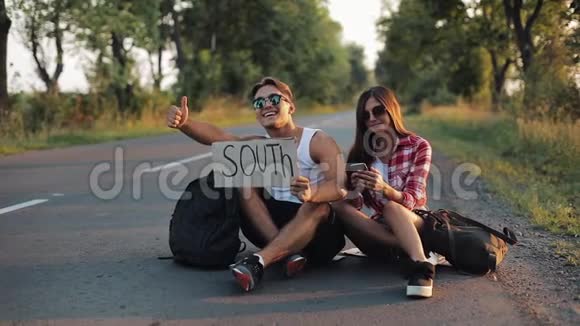 一对年轻夫妇坐在路上搭便车使用智能手机一男一女在高速公路上停车视频的预览图