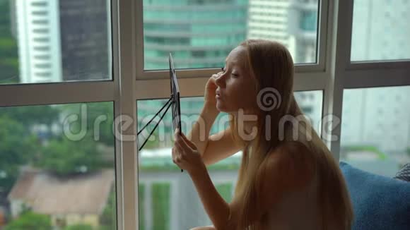 一位年轻女子在市中心的一扇全景窗旁化妆的超慢动作镜头视频的预览图