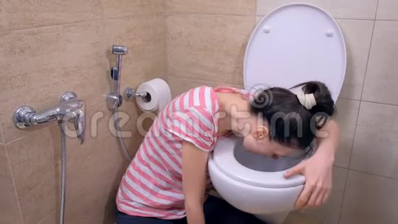 年轻的孕妇疲惫的女人在坐在家里地板上的厕所里呕吐视频的预览图