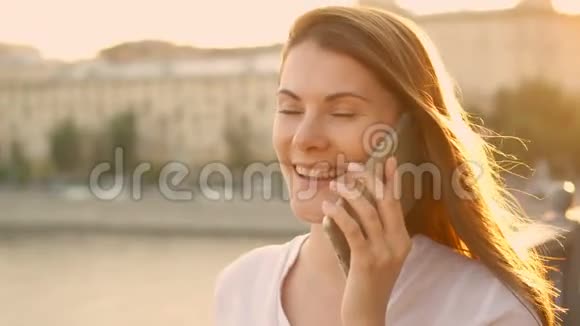 快乐的年轻女人在户外放松漂亮的女孩在她的智能手机上说话夏日阳光灿烂视频的预览图