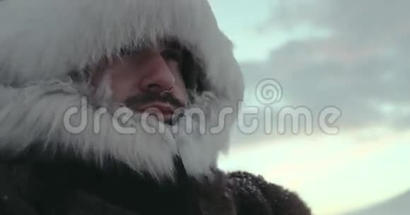 一幅穿着传统驯鹿外套的站立男子在寒冷的冬天蒸汽和看着特写北极考察视频的预览图