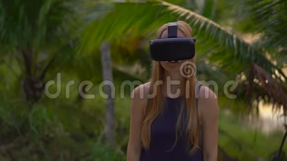 一位美丽的年轻女子的特写镜头在热带公园里使用VR耳机一个戴着虚拟现实眼镜的人感觉他视频的预览图