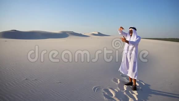 年轻的阿拉伯阿联酋酋长寻找美丽的框架站在广阔的沙漠中清澈见底视频的预览图