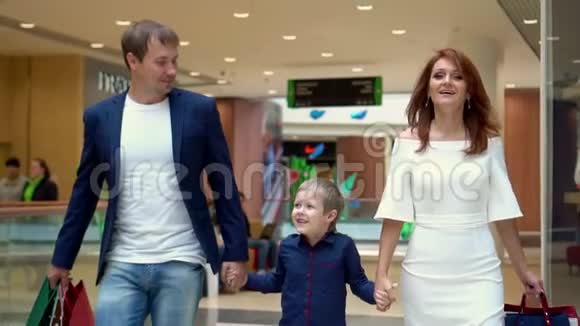 这个男孩高兴地举起父母的手一家人带着销售袋穿过购物中心小小的视频的预览图