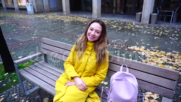 冬天坐在城市户外的长凳上微笑着看着镜头的幸福年轻女人的肖像视频的预览图