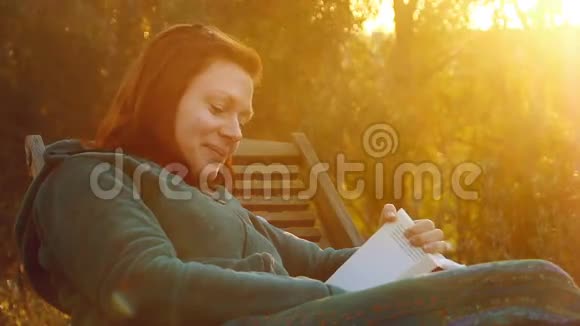 年轻美丽的微笑女子在躺椅上放松在夕阳的余晖下看书视频的预览图