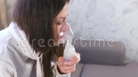 使用雾化器和吸入器进行治疗年轻女性通过吸入面罩吸入特写面部侧视视频的预览图