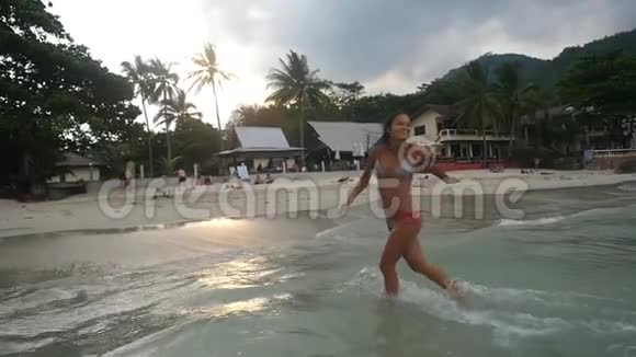 美丽的年轻美女在热带海滩上奔跑在日落时泼水享受假期慢慢慢慢视频的预览图