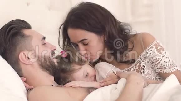一家人在床上微笑年轻的母亲亲吻着她的小女儿视频的预览图