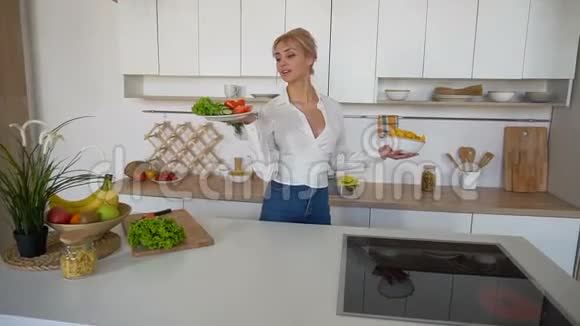 可爱的女孩摆姿势拿着盘子沙拉和薯片脸上带着微笑站在现代美食的中间视频的预览图