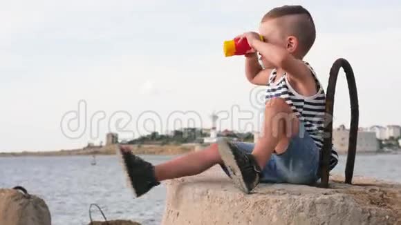 可爱的小男孩带着望远镜坐在海边的防波堤上视频的预览图