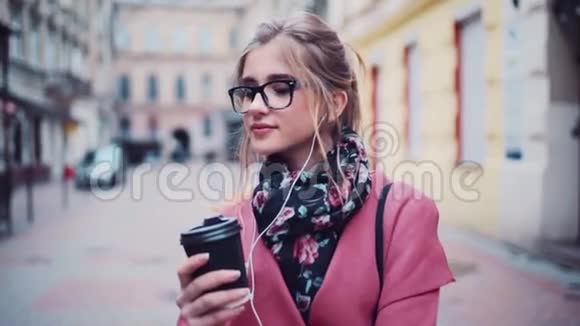 美丽的金发女孩有着天然的妆容和轻盈的配饰带着耳机手里拿着热咖啡视频的预览图