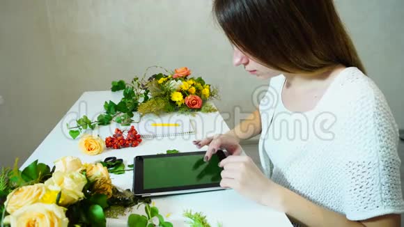 妩媚的花艺师在编花的时候与pla坐在同一桌看着平板电脑的流行趋势视频的预览图