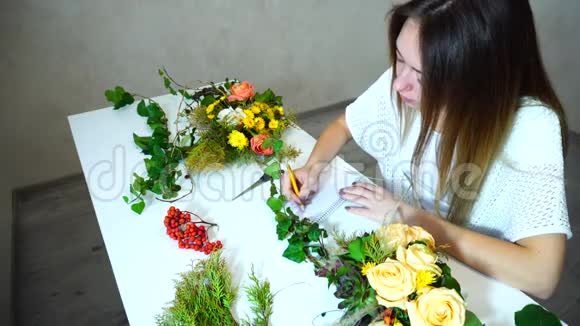 年轻的女性花处理者保存花的记录并在办公室坐在桌子上的笔记本上写观察视频的预览图