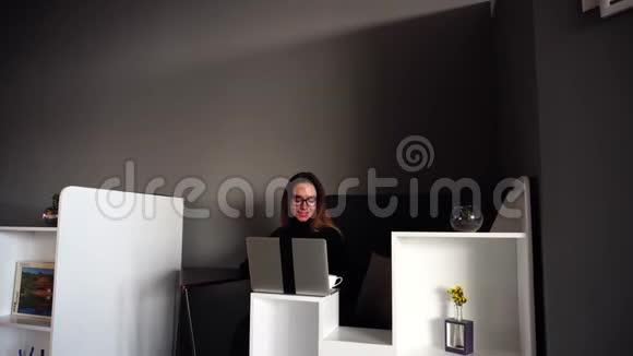 在现代办公室里坐在电脑前坐在桌子旁一位令人惊叹的女办公室工作人员微笑着看镜头尝试咖啡视频的预览图