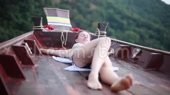 穿比基尼日光浴的年轻女子躺在海里的一艘船上1920x1080视频的预览图
