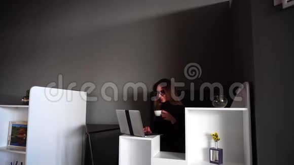 迷人的女记者在电脑工作喝咖啡下午坐在现代办公室的桌子上视频的预览图