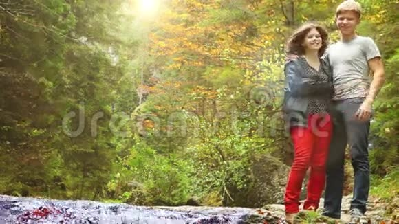 在宁静的秋日年轻的一对夫妇站在森林山溪附近照相机开始逐渐缩小视频的预览图