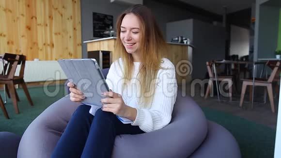 女孩手拿着平板电脑为自己寻找有趣的信息坐在软椅子上在不寻常的咖啡馆里视频的预览图