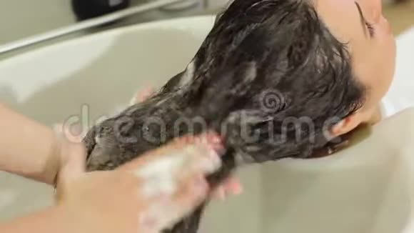 理发师在美容院理发前洗一个年轻女孩的头发视频的预览图