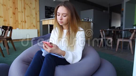 美丽的女孩写短信在沮丧的感觉借助移动坐在软椅子上在不寻常的咖啡馆在冬天的一天视频的预览图