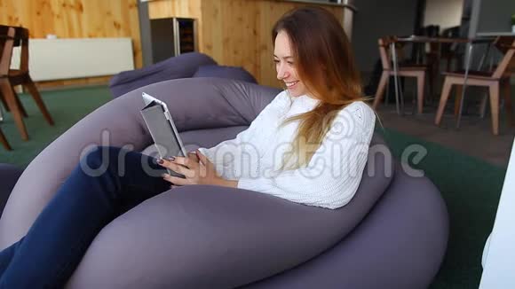 现代女性开车在平板电脑上玩游戏冬天坐在现代咖啡馆的软椅子上视频的预览图