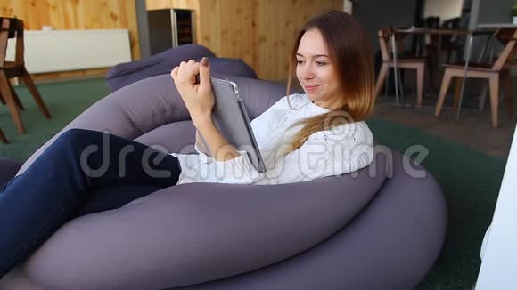 在时尚咖啡馆里坐在软椅上开着触摸屏小玩意感冒打喷嚏的女孩的肖像视频的预览图