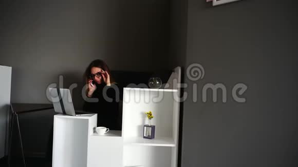 作家女孩在笔记本电脑键盘上打印在手机上交谈白天坐在现代咖啡馆或办公室的桌子上视频的预览图
