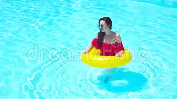 美丽的年轻女子在游泳池里放松豪华酒店室外游泳池的女孩带充气橡胶圈视频的预览图