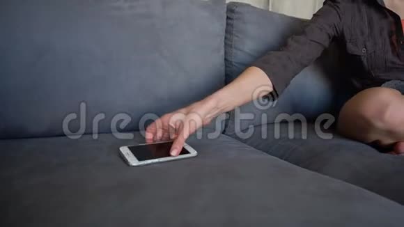 漂亮的女孩伸手接电话接来电坐在灰色客厅里铺着毯子的柔软沙发上视频的预览图