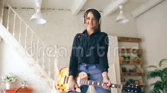 在室内的家庭工作室里戴着耳机摆着电吉他的美丽年轻微笑女孩视频的预览图