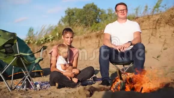一个年轻的家庭有一个孩子夏天坐在篝火旁靠近帐篷视频的预览图