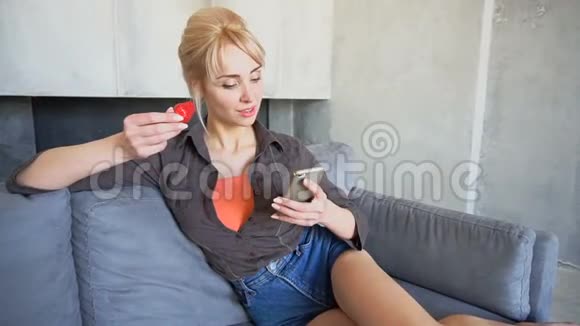 一幅美丽的女人的肖像她走在触摸屏手机上试着吃成熟的草莓坐在柔软的地上视频的预览图