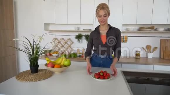 可爱的女性摆姿势和微笑的相机与成熟的草莓盘子在现代厨房视频的预览图