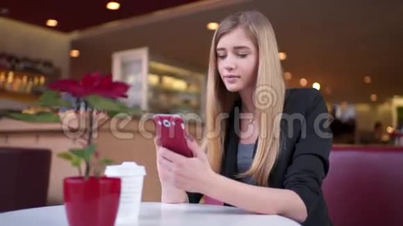 美丽的女人坐在咖啡馆里A和一个朋友在她的智能手机上发短信她对她的回答感到惊讶视频的预览图