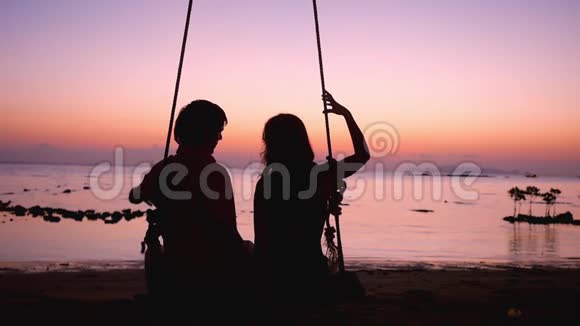 海上度假夕阳和爱在秋千上在令人惊叹的日落中一对情侣从怀里剪下了心的轮廓视频的预览图