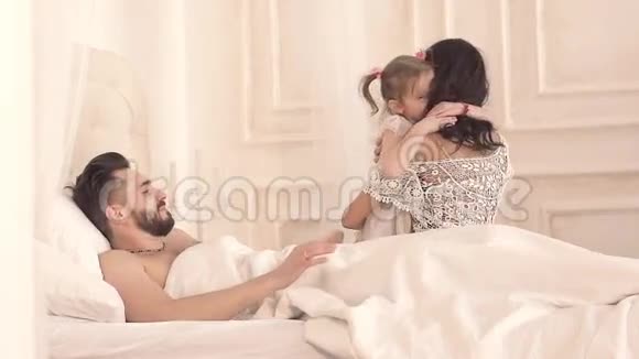 幸福的三口之家母亲父亲和女儿在床上玩视频的预览图