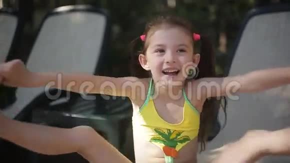 一个穿着泳衣的小女孩正坐在游泳池旁的休息室里笑着视频的预览图