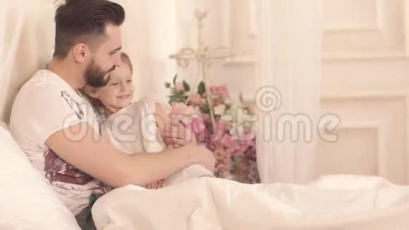 阳光明媚的早晨小女孩和父亲在床上玩得开心的画像视频的预览图