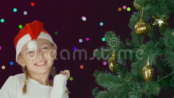 圣诞老人戴着红帽子在圣诞树旁跳舞的快乐少女快乐的年轻白种人女孩接近装饰的圣诞节视频的预览图