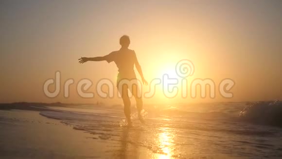 快乐的小女孩快乐地跳在靠近海边的海滩上金色的夕阳上波涛汹涌高清1920x1080慢动作视频的预览图