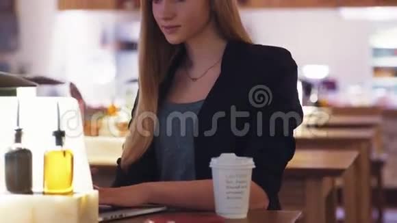 穿黑色夹克的漂亮女孩坐在咖啡馆A商店里她把注意力集中在笔记本上视频的预览图