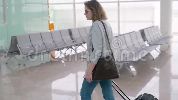 机场里的一个金发女郎带着滚动的行李箱包走路视频的预览图