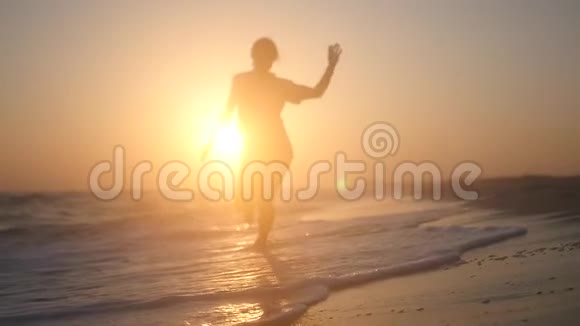 日落时一个快乐苗条的女孩在浪花中奔跑高清1920x1080慢动作视频的预览图