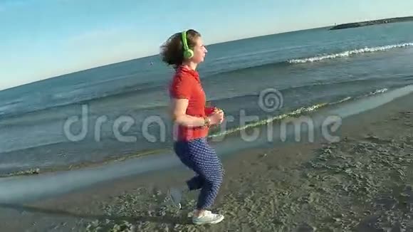 女孩戴着绿色耳机在海滩上奔跑视频的预览图