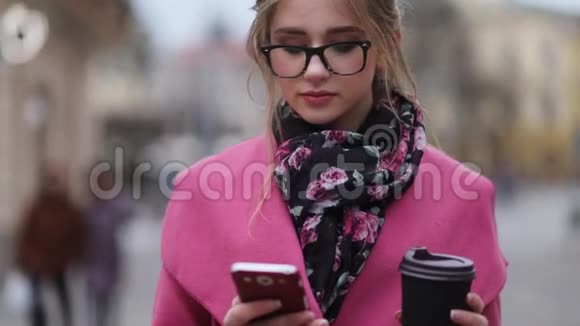 可爱的女孩穿着时髦的服装站在市中心喝杯咖啡发短信很忙城市视频的预览图